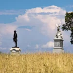 Two statues in a grassy field under a blue sky with clouds.