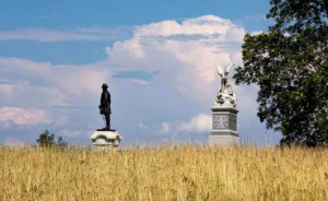 Two statues in a grassy field under a blue sky with clouds.