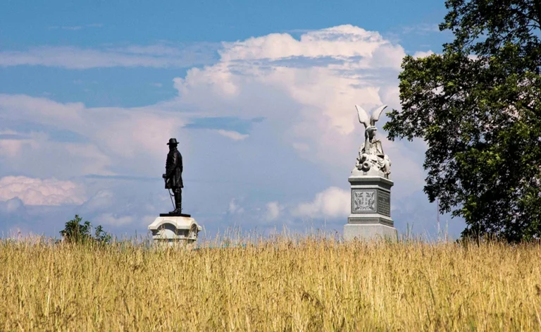 Two statues in a grassy field under a blue sky with clouds.
