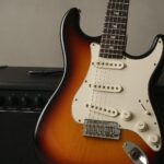 Electric guitar positioned against an amplifier with a neutral backdrop