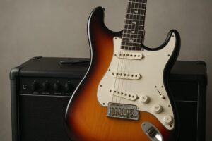 Electric guitar positioned against an amplifier with a neutral backdrop