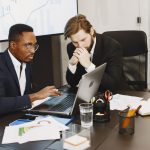 Two businessmen engaged in a strategy meeting with laptops and charts. — Adulting Done Right: Your Ultimate Destination for S
