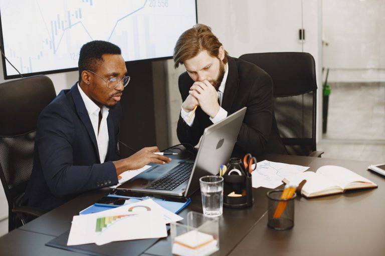 Two businessmen engaged in a strategy meeting with laptops and charts. — Adulting Done Right: Your Ultimate Destination for S