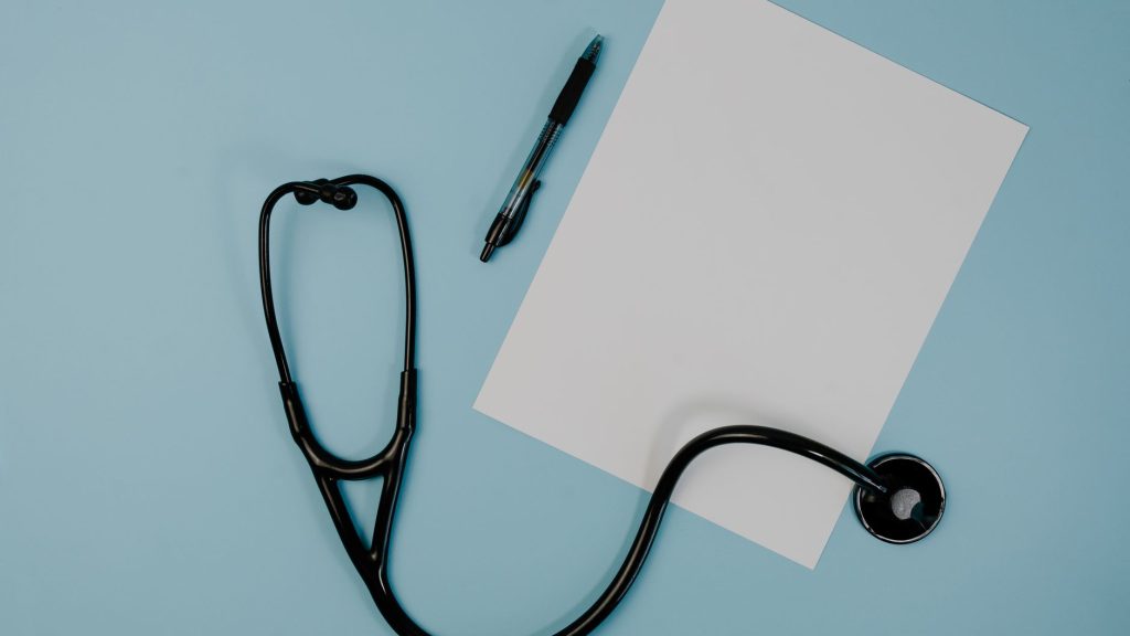 Flat lay of stethoscope, blank paper, and pen on blue surface — Before and After Invisalign Results: Realistic Expectations