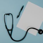 Flat lay of stethoscope, blank paper, and pen on blue surface — Before and After Invisalign Results: Realistic Expectations