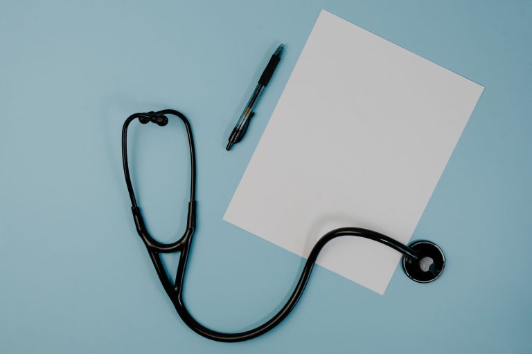 Flat lay of stethoscope, blank paper, and pen on blue surface — Before and After Invisalign Results: Realistic Expectations