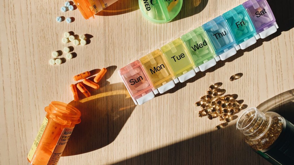 Colorful pill organizer with medication bottles and tablets on a wooden surface. — Flexible Recovery Plans with Outpatient Re