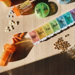 Colorful pill organizer with medication bottles and tablets on a wooden surface. — Flexible Recovery Plans with Outpatient Re