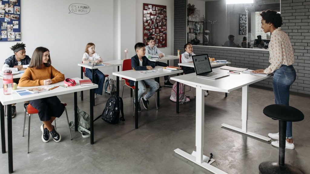 A diverse group of students attentively listens to a teacher in a modern classroom setting. — Fulfill Your Passion: Teaching