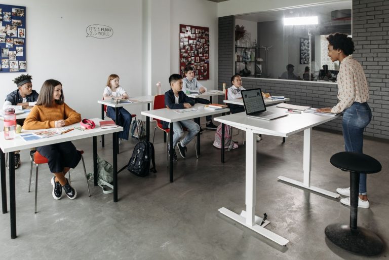A diverse group of students attentively listens to a teacher in a modern classroom setting. — Fulfill Your Passion: Teaching