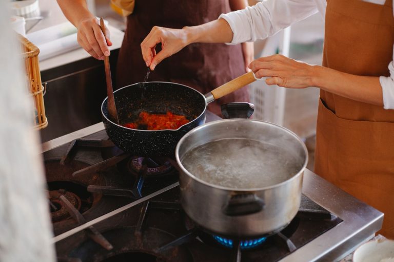 Close-up of two women cooking; stirring sauce and boiling water on stove. — Mediterranean Magic: Burst Cherry Tomato & Ro