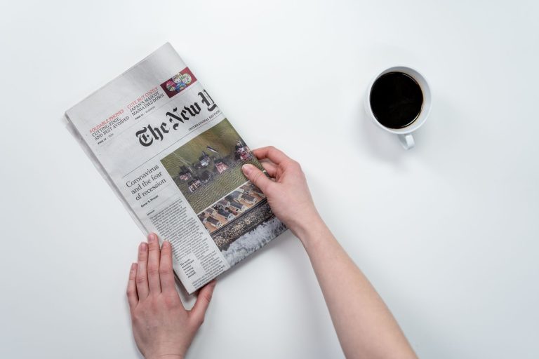 Flat lay of hands holding The New York Times newspaper with coffee on a white table. — The Legalities of Buying Weed Online