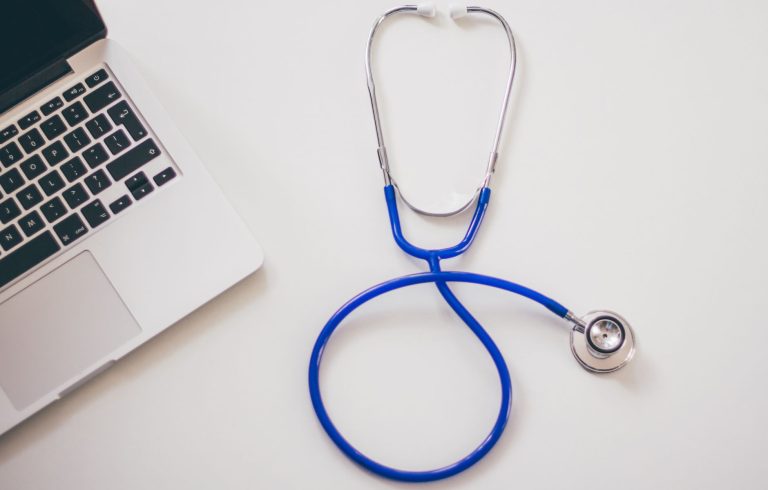 Medical stethoscope and laptop on a white desk, symbolizing digital health solutions. — Understanding the Cost of Facial Fat