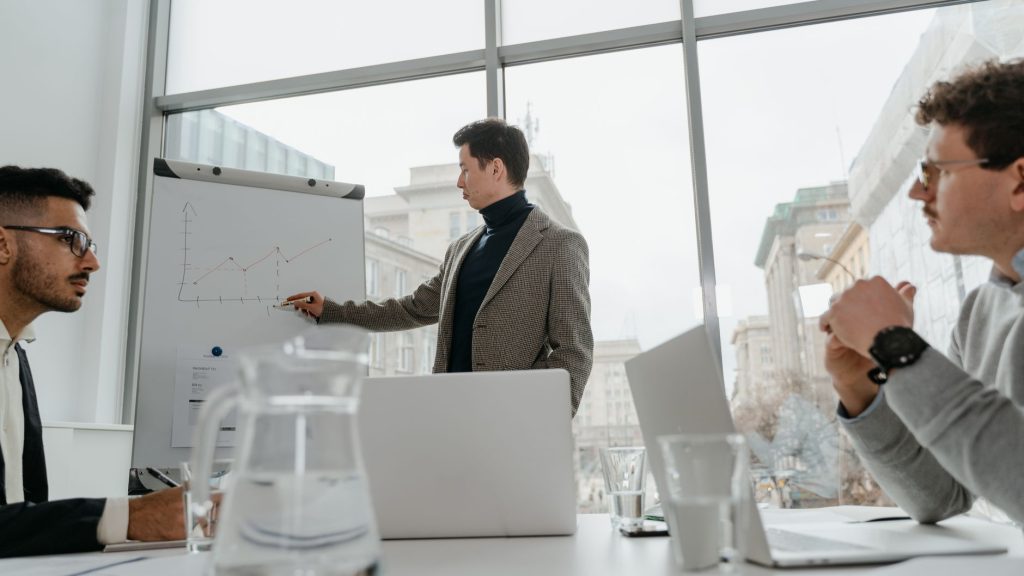 Professionals engaged in a collaborative business meeting with charts and laptops in a modern office setting. — Unlock Expert