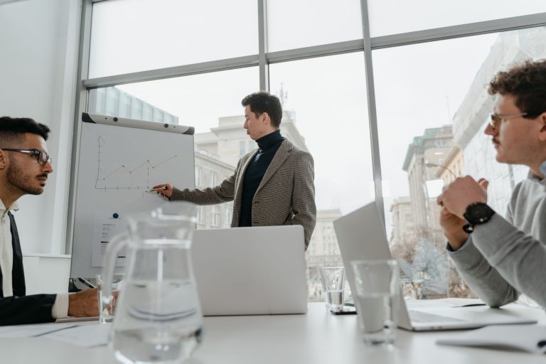 Professionals engaged in a collaborative business meeting with charts and laptops in a modern office setting. — Unlock Expert