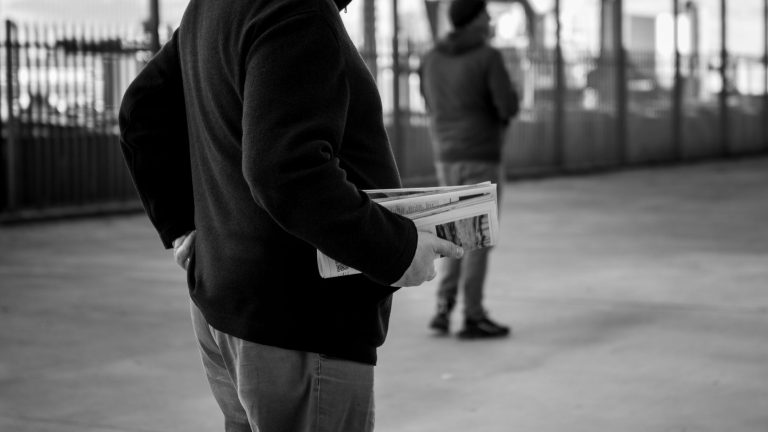 A monochrome image of a person holding newspapers in an urban environment, capturing the essence of street life. — Vavada reg